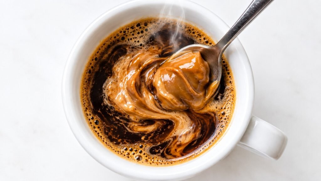 Biscoff cookie butter being stirred into hot espresso in a small white cup